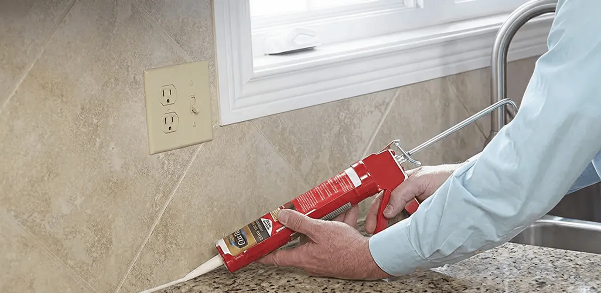 Handyman applying caulk along a kitchen backsplash and countertop seam in Miami, FL
