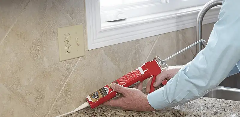 Handyman applying caulk along a kitchen backsplash and countertop seam in Miami, FL